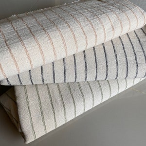 May include: Three striped fabric swatches stacked on top of each other. The top swatch is beige with brown stripes, the middle swatch is beige with black stripes, and the bottom swatch is beige with green stripes.