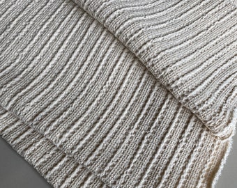 Può includere: Primo piano di un tessuto a maglia color crema con un motivo testurizzato e a coste.
