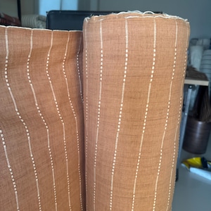 May include: Two rolls of brown fabric with white vertical stripes. The fabric has a subtle texture and a slightly distressed look.