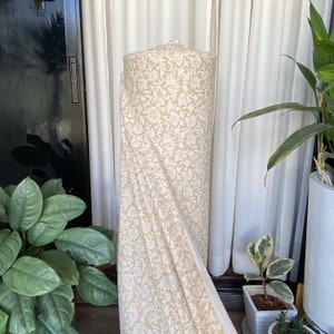 May include: A roll of white fabric with a beige floral pattern. The fabric is folded and draped over a surface.