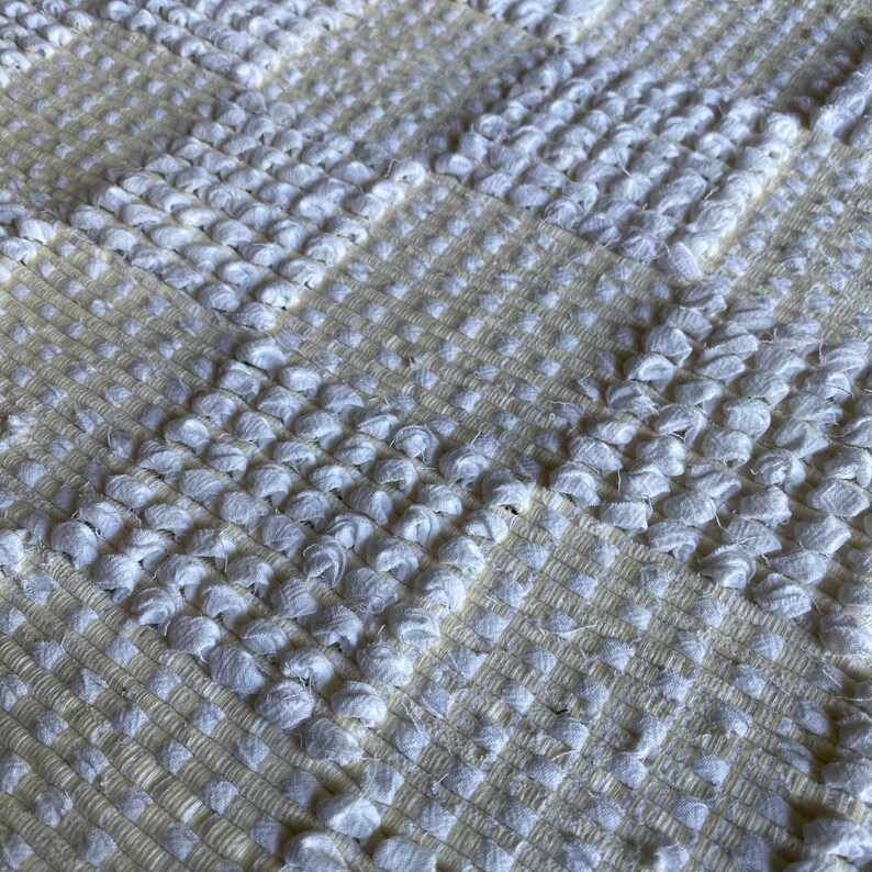 Pode incluir: Tapete branco tecido com um design texturizado em la&ccedil;o. O tapete tem um padr&atilde;o xadrez sutil.