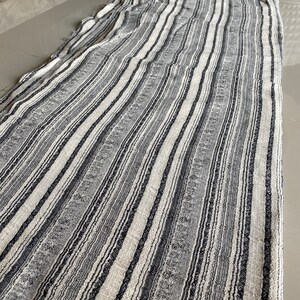 May include: A white and black striped fabric with a textured weave. The fabric has a subtle sheen and a slightly rough texture.