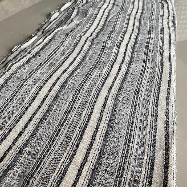 May include: A white and black striped fabric with a textured weave. The fabric has a subtle sheen and a slightly rough texture.
