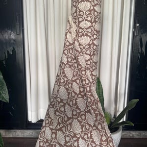 May include: A roll of brown fabric with a white floral pattern. The fabric is folded and draped over a surface.
