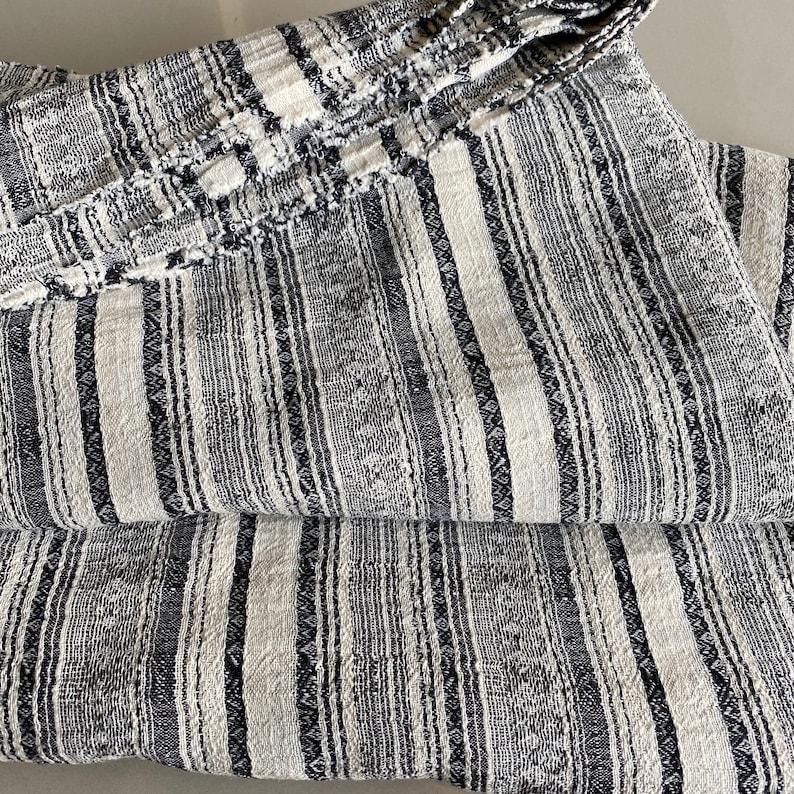 May include: A black and white striped fabric with a textured weave. The fabric is folded in thirds, showing the pattern.