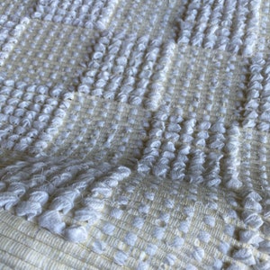 Pode incluir: Tapete branco tecido com um padr&atilde;o texturizado em relevo. O tapete tem um design xadrez com uma cor bege sutil.