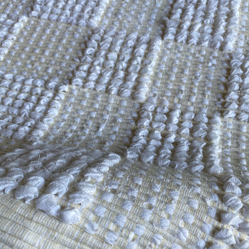 Pode incluir: Tapete branco tecido com um padr&atilde;o texturizado em relevo. O tapete tem um design xadrez com uma cor bege sutil.