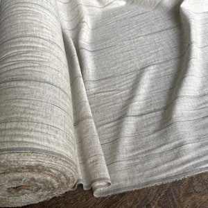 May include: A roll of off-white fabric with thin black stripes. The fabric is woven and has a slightly textured surface.