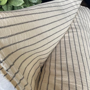 May include: Two pieces of off-white fabric with black stripes. The fabric is folded in half, showing the stripes running in two directions.