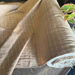May include: A roll of brown fabric with a white grid pattern. The fabric is soft and has a slightly textured surface.