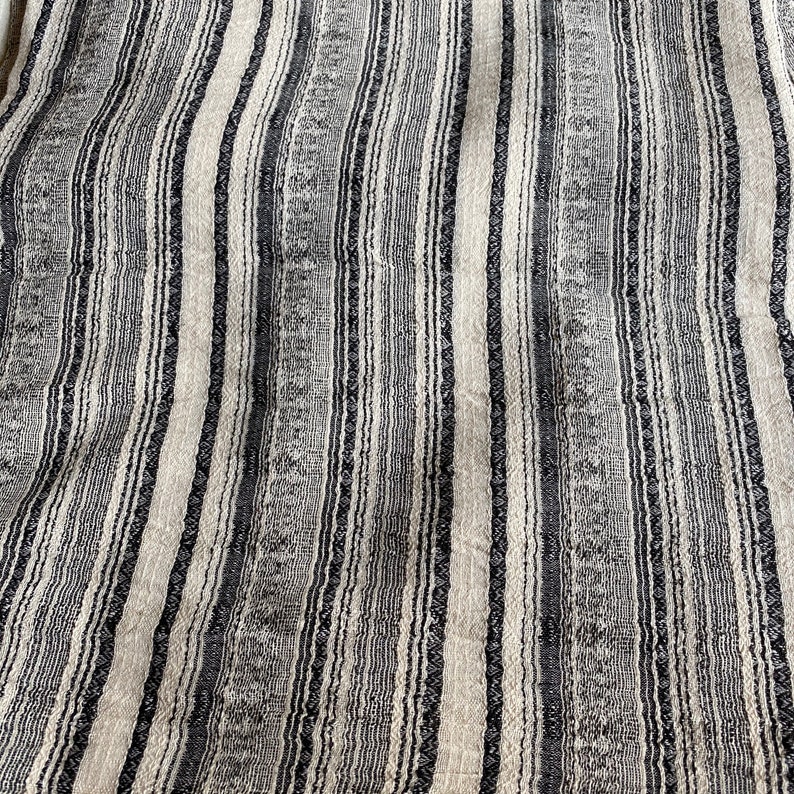 May include: Close-up of a woven fabric with alternating black and white stripes. The fabric has a textured, slightly rough surface.