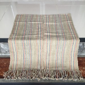 May include: A woven throw blanket with a fringe border. The blanket is made of a natural fiber and has a striped pattern in shades of brown, blue, and orange.
