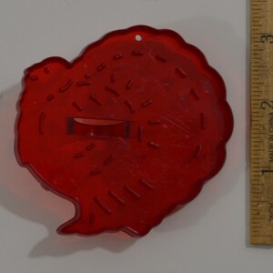 May include: Red plastic turkey-shaped cookie cutter. The cutter has a detailed design of feathers and a small hole in the top for hanging.