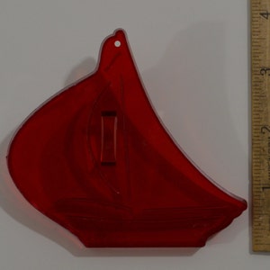May include: Red plastic cookie cutter shaped like a sailboat. The cutter is about 3 inches tall.
