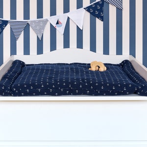 May include: White changing table with a blue and white changing pad with anchor print. A wooden toy is on the changing pad.