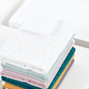 Peut inclure: Une pile de couvertures pour bébé blanches, bleu sarcelle, roses, vertes, jaune moutarde et grises avec des pois dorés. La couverture du dessus a un patch en éponge blanche.