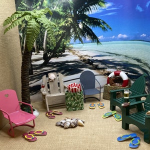 May include: A miniature beach scene with a pink, green, and gray chairs, a palm tree, a life preserver, a wicker basket, and flip flops on a sandy surface.