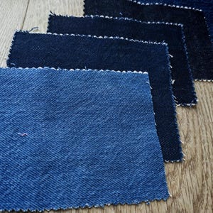 May include: A selection of denim fabric swatches in various shades of blue. The samples are arranged diagonally, displaying the different textures and colours of the denim material. The edges of the fabric are frayed.