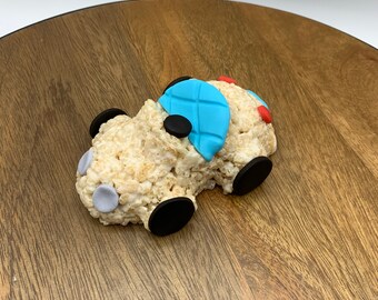 Pode incluir: Um doce de arroz em forma de carro azul e branco com rodas pretas e detalhes cinzentos e vermelhos.