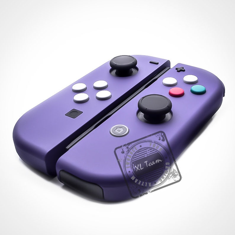 Puede incluir: Mandos Joy-Con Nintendo Switch de color morado con botones blancos y un logotipo XL Team negro. Los mandos est&aacute;n en posici&oacute;n cerrada.