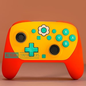 Könnte beinhalten: Ein gelb-roter Videospiel-Controller mit Blumendesign und türkisfarbenen Knöpfen. Der Controller hat ein Steuerkreuz, Aktionstasten und Steuerknüppel. Der Text "XL TEAM CONTROLLERS" befindet sich unten.