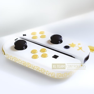 K&ouml;nnte beinhalten: Wei&szlig;er und gelber Nintendo Switch-Controller mit schwarzen Kn&ouml;pfen und einem floralen Design. Der Controller hat den Text "XL TEAM CONTROLLERS" auf der Seite.