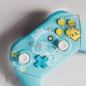 May include: A light blue Nintendo Switch controller with a white and yellow design featuring a cartoon character. The controller has a white plus button, a white minus button, and a white home button. The controller also has a white analog stick and a white d-pad.