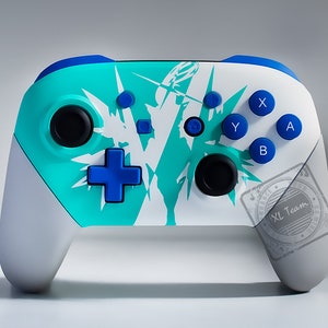 Könnte beinhalten: Ein weißer und blaugrüner Nintendo Switch-Controller mit blauen Knöpfen und einem weißen und blaugrünen Grafikdesign. Der Controller hat ein schwarzes XL Team-Logo auf der rechten Seite.