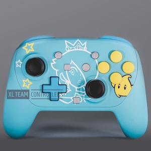 May include: A light blue video game controller featuring a white line art illustration of a character with a crown, yellow star graphics, and a yellow Luma character. The controller includes black joysticks, yellow buttons, and the text XL TEAM CONTROLLERS.
