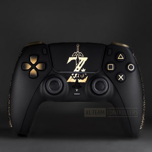 May include: A black PlayStation 5 DualSense controller with gold accents. The controller features a custom design with a gold Triforce symbol and the text "XL TEAM CONTROLLERS".