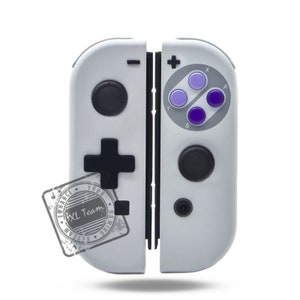 May include: A white Nintendo Switch controller with a gray and black Super Nintendo style button layout. The controller has a black plus button and a black minus button. The controller has a black and white sticker on the left side that says "Enhance Your Gaming XL Team".