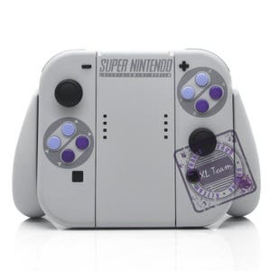 May include: A gray and white handheld gaming console with a Super Nintendo logo and buttons. The console has a gray and purple button pad on the left and right sides.