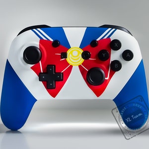 May include: A white Nintendo Switch controller with a blue and white Sailor Moon design. The controller has a red bow with a yellow center and a black D-pad.