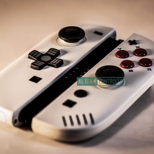 May include: White gaming controller with black and red buttons. The controller has a D-pad, analog stick, and action buttons. The text "XL TEAM CONTROLLER" is visible on the controller.