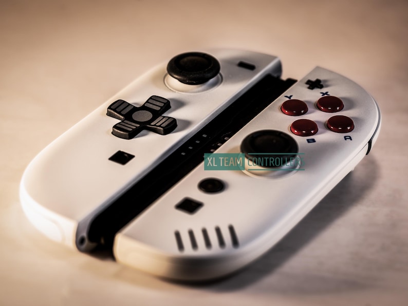May include: White gaming controller with black and red buttons. The controller has a D-pad, analog stick, and action buttons. The text "XL TEAM CONTROLLER" is visible on the controller.