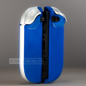 Puede incluir: Un mando de juego azul y plateado con un dise&ntilde;o elegante. El mando tiene un acabado azul brillante con detalles plateados en la parte superior y los laterales. El texto "XL TEA CONTROLLERS" est&aacute; impreso en el lateral.