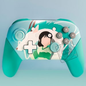 Könnte beinhalten: Ein türkisfarbener Nintendo Switch-Controller mit einem benutzerdefinierten Design, das eine weiße und blaue Kreatur und ein Mädchen mit langen schwarzen Haaren zeigt. Der Controller hat die Standardtasten mit den Bezeichnungen X, Y, A und B.