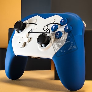 May include: A blue and white video game controller with a white faceplate and blue accents. The controller has a black D-pad, two black analog sticks, and four blue buttons labeled A, B, X, and Y. The controller also has a white button labeled "XL Team Gaming".