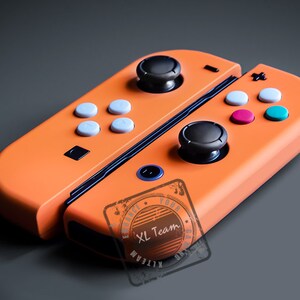 May include: Orange Nintendo Switch Joy-Con controllers with black buttons and a blue trim. The controllers have a custom design with a black and white stamp that says "XL Team".