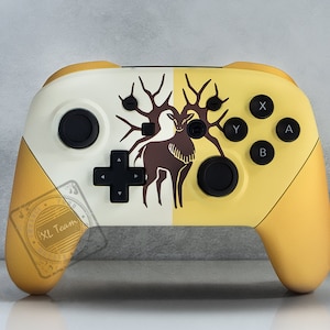 May include: A custom-designed Nintendo Switch controller with a white and yellow color scheme. The controller features a stylized deer with antlers on the front, and the text "XL Team" is visible on the left side.
