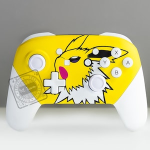 May include: A yellow and white Nintendo Switch controller with a Pikachu design. The controller has a yellow background with a white Pikachu graphic in the center. The controller has white buttons and a white joystick.