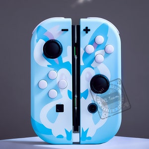 May include: A light blue Nintendo Switch controller with a white and light blue patterned design. The controller has a white button layout and a black XL Team logo.