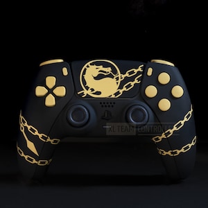 Puede incluir: Mando de videojuegos negro con detalles dorados. El mando presenta botones dorados, un emblema de dragón dorado y detalles de cadena dorada. El texto "RL TEAM CONTROLS" es visible en la parte inferior del mando.