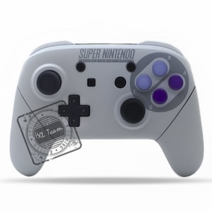 Może przedstawiać: Biały kontroler Nintendo Switch z designem Super Nintendo Entertainment System. Kontroler ma fioletowe i niebieskie przyciski oraz czarny krzyż kierunkowy.