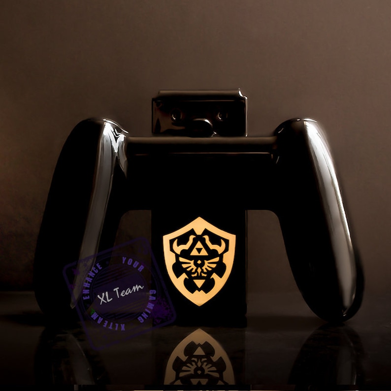May include: Black Nintendo Switch console stand with two black Joy-Con controllers and a gold Triforce shield design. The stand is labeled "XL Team Gaming" in a purple circle.