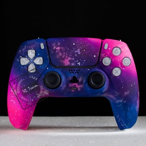 May include: A custom-painted pink and blue PlayStation 5 controller with a galaxy design. The controller has a white logo and the words "XL Team" on the left side.