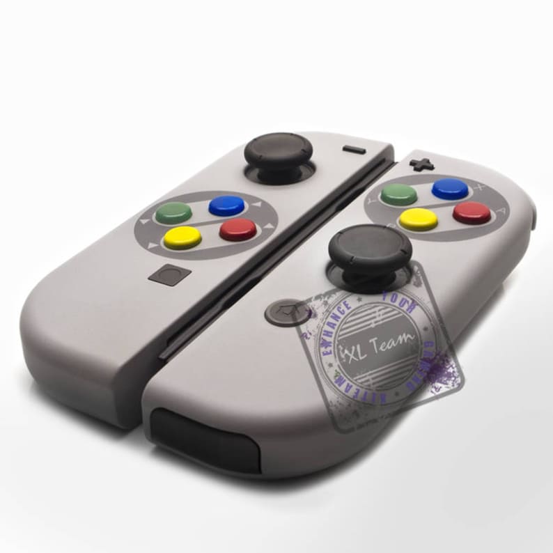 May include: A gray Nintendo Switch controller with a Super Nintendo design. The controller has a gray and black color scheme with colorful buttons. The controller has a stamp that says "Enhance Your Game" with the text "IXL Team" inside the stamp.
