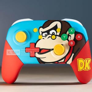 Könnte beinhalten: Ein blauer, roter und gelber Nintendo Switch-Controller mit einem Donkey Kong-Design. Der Controller zeigt auf der Vorderseite ein großes Bild von Donkey Kongs Gesicht sowie den Text "DK" auf der rechten Seite.