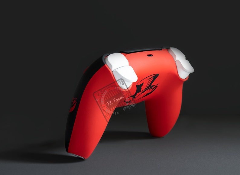 May include: A red and black video game controller with white buttons. The controller features a black graphic design on the front and side. The controller is designed for gaming.