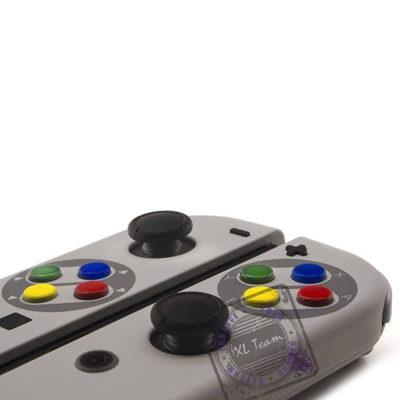May include: A gray and white video game controller with black buttons and a red, yellow, blue, and green button layout. The controller is split in half and has a black joystick on each side.